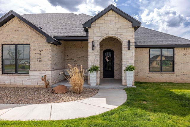 property entrance with a shingled roof, brick siding, and a yard