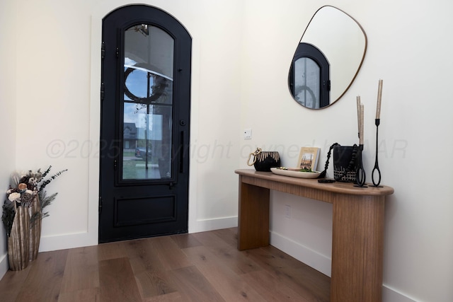 entrance foyer with arched walkways, wood finished floors, and baseboards