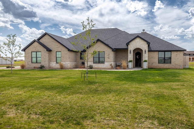 french provincial home featuring brick siding, roof with shingles, and a front lawn