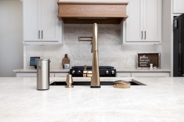 kitchen with light stone countertops, white cabinets, and range hood