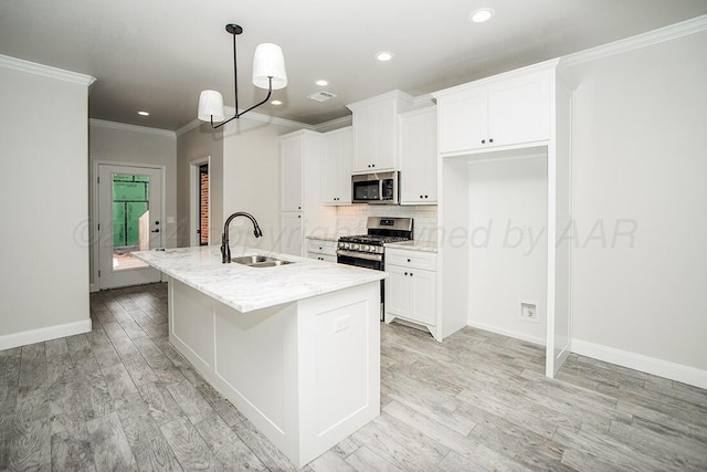 kitchen featuring a kitchen island with sink, stainless steel appliances, a sink, white cabinetry, and backsplash