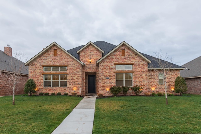 view of front of house featuring brick siding, a front lawn, and roof with shingles
