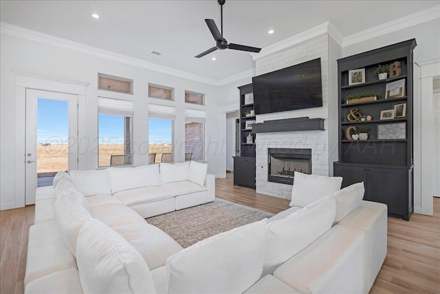 living room with crown molding, ceiling fan, a stone fireplace, and light hardwood / wood-style flooring