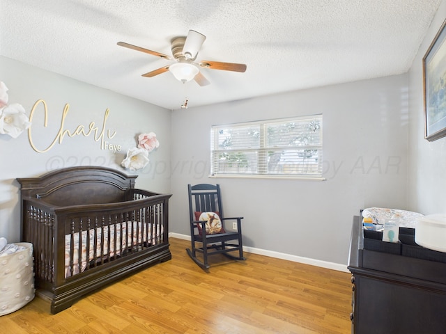1409 Bailey Ave, Dumas, TX 79029 - bedroom with light wood-type flooring, a nursery area, a textured ceiling, and a ceiling fan