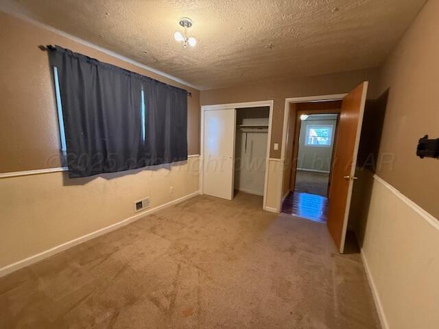 unfurnished bedroom featuring carpet flooring, a textured ceiling, baseboards, visible vents, and a closet