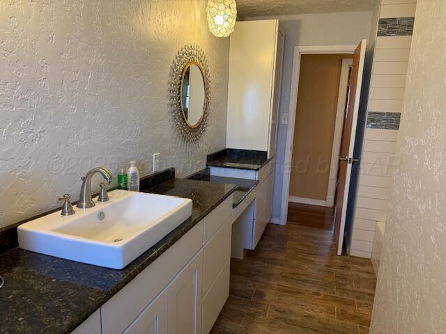 full bathroom with a textured wall, vanity, and wood finished floors