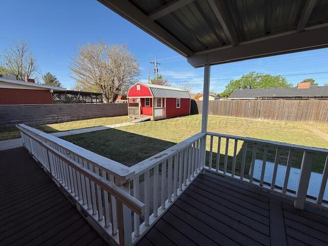 wooden terrace featuring a lawn, an outdoor structure, a shed, and a fenced backyard