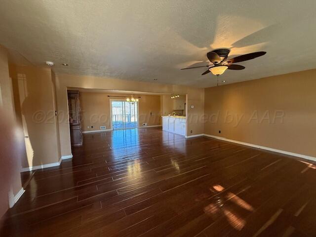 spare room with ceiling fan with notable chandelier, wood finished floors, baseboards, and a textured ceiling
