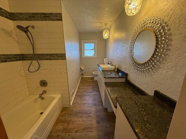 bathroom with a textured ceiling, toilet, wood finished floors, a textured wall, and vanity