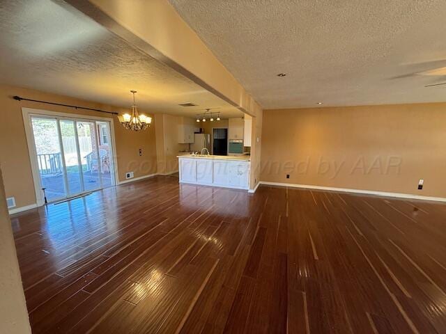 unfurnished living room featuring dark wood-style flooring, a textured ceiling, baseboards, and a notable chandelier
