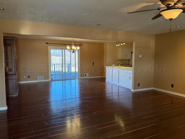 empty room featuring ceiling fan with notable chandelier, baseboards, dark wood-style floors, and visible vents