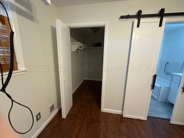 corridor with a barn door, baseboards, wood finished floors, and visible vents