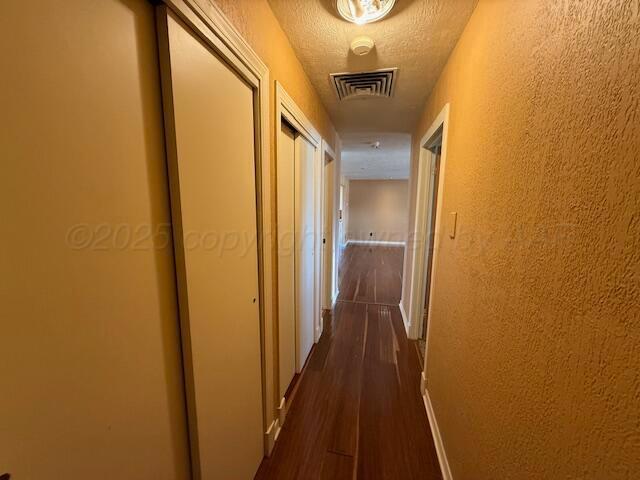 hallway featuring dark wood-style flooring, a textured wall, visible vents, and a textured ceiling
