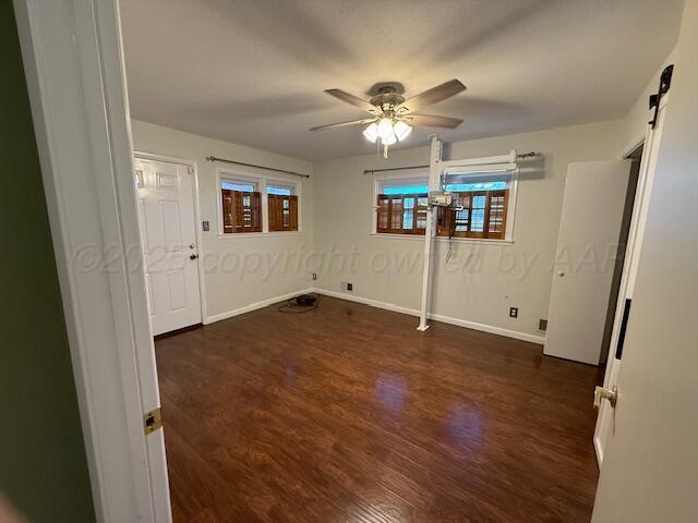 unfurnished bedroom featuring a ceiling fan, baseboards, a barn door, and dark wood finished floors