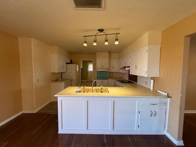 kitchen featuring a sink, oven, baseboards, a peninsula, and white cabinetry