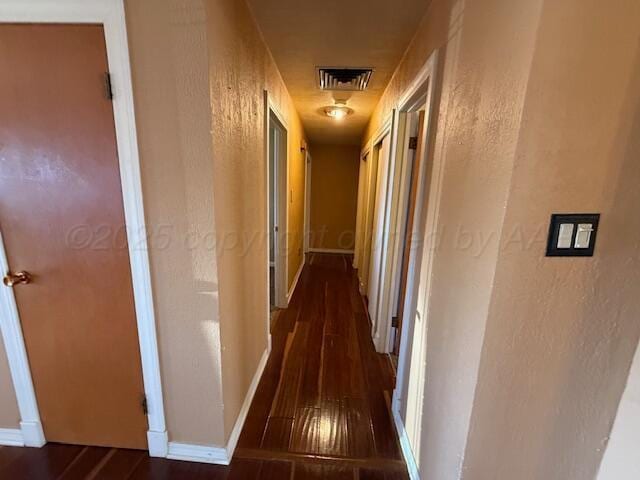 hall featuring hardwood / wood-style floors, baseboards, visible vents, and a textured wall