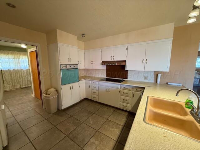 kitchen with light countertops, wall oven, under cabinet range hood, and a sink