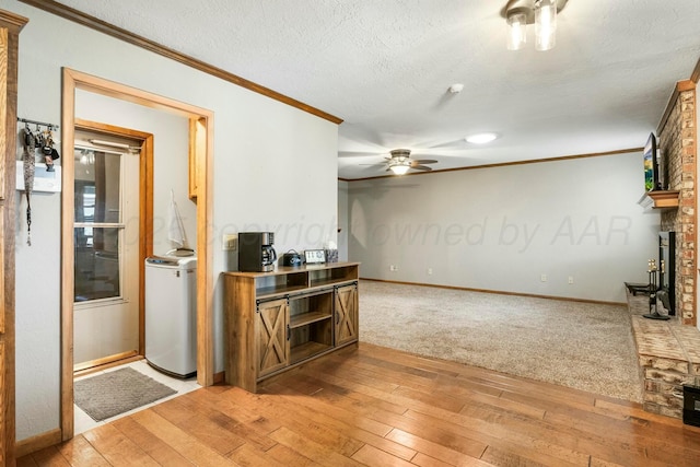 living area with crown molding, a textured ceiling, ceiling fan, light wood-style flooring, and a fireplace