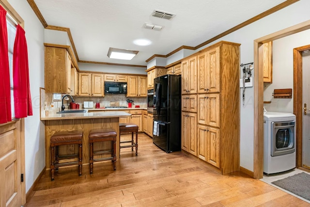 kitchen featuring crown molding, a sink, light wood-style flooring, washer / dryer, and black appliances