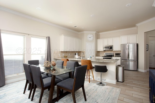 dining room with sink, crown molding, and light hardwood / wood-style flooring