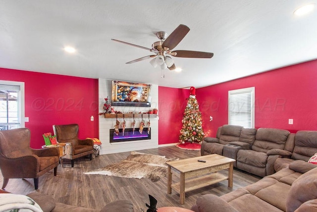 living area with ceiling fan, an accent wall, a fireplace, and wood finished floors