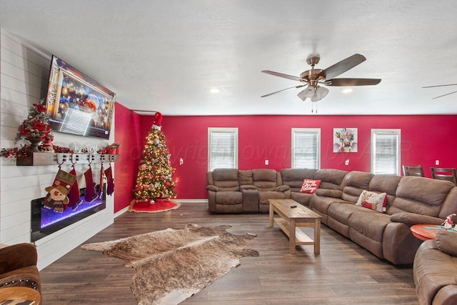 living area with a warm lit fireplace, wood finished floors, a ceiling fan, and baseboards