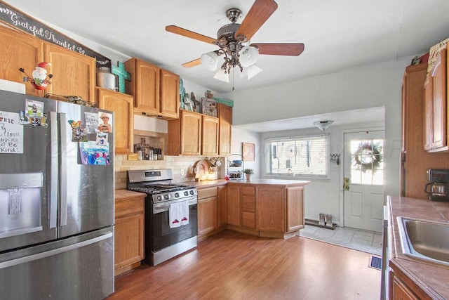 kitchen featuring light wood finished floors, tasteful backsplash, brown cabinets, a peninsula, and stainless steel appliances