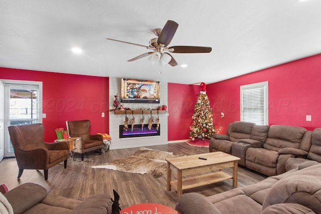 living area featuring a glass covered fireplace, ceiling fan, an accent wall, wood finished floors, and recessed lighting