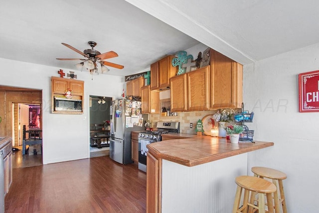 kitchen with stainless steel appliances, tile counters, brown cabinetry, a peninsula, and a kitchen bar