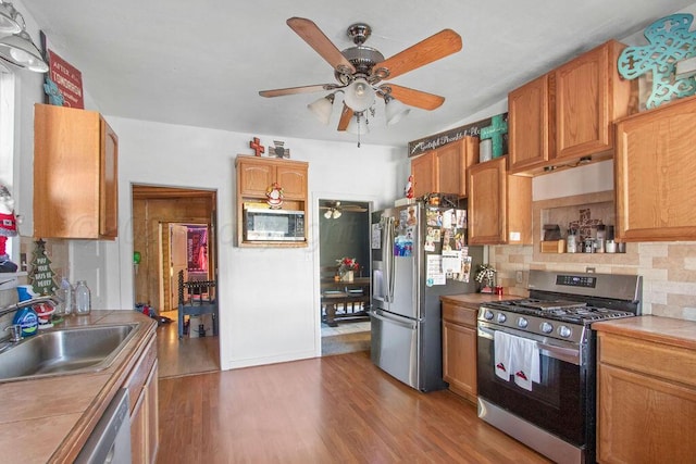 kitchen featuring stainless steel appliances, tile counters, tasteful backsplash, a sink, and wood finished floors