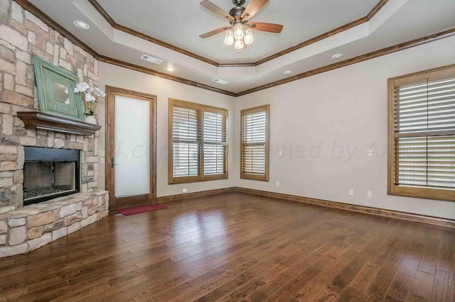 unfurnished living room featuring crown molding, a stone fireplace, dark hardwood / wood-style floors, a tray ceiling, and ceiling fan