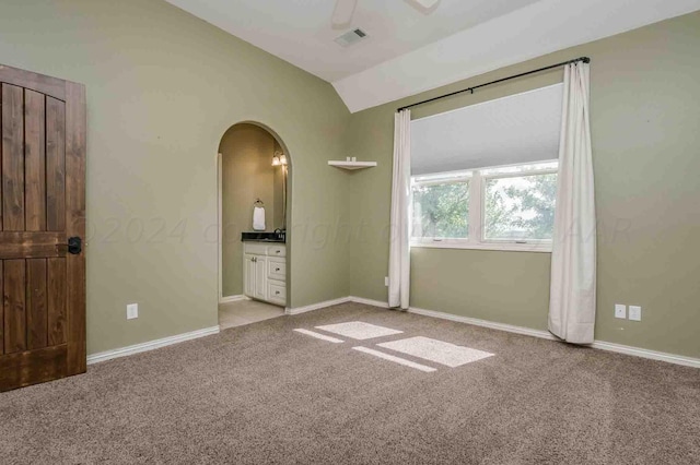 unfurnished bedroom featuring connected bathroom, lofted ceiling, ceiling fan, and light carpet