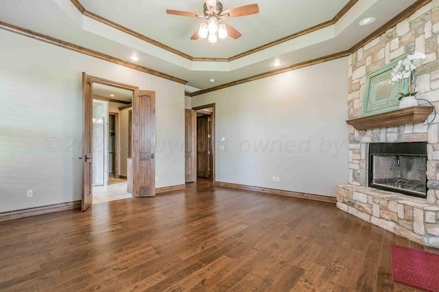 unfurnished living room with ornamental molding, a fireplace, dark hardwood / wood-style floors, a tray ceiling, and ceiling fan