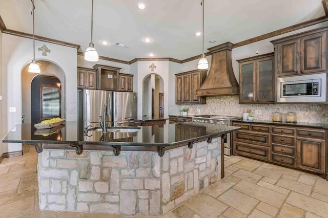 kitchen featuring appliances with stainless steel finishes, premium range hood, a large island with sink, and a kitchen breakfast bar