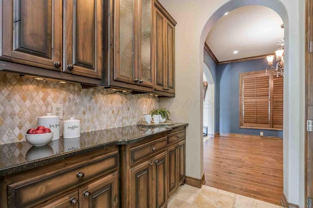 kitchen with dark stone counters, a chandelier, tasteful backsplash, ornamental molding, and light hardwood / wood-style flooring