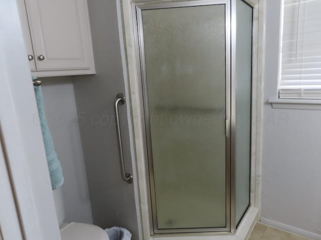 bathroom featuring a stall shower, baseboards, tile patterned floors, and toilet