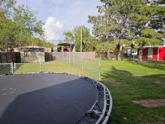 view of yard with a trampoline, a shed, a fenced backyard, an outbuilding, and a detached carport