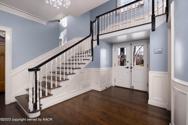 entrance foyer with ornamental molding, dark wood-type flooring, an inviting chandelier, and french doors