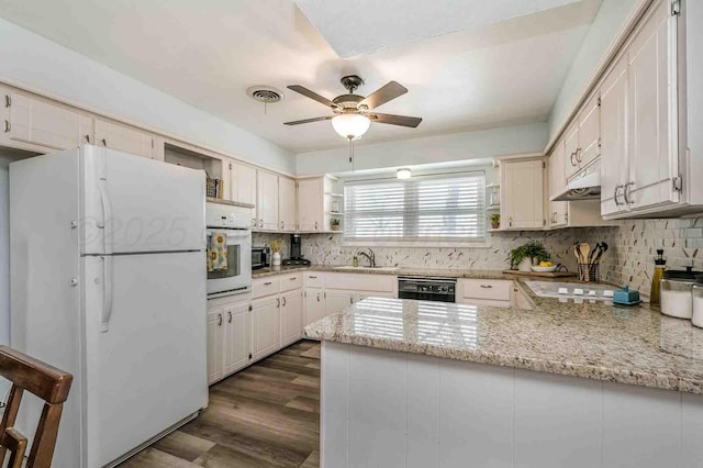 kitchen with kitchen peninsula, dark wood-type flooring, light stone counters, white appliances, and decorative backsplash