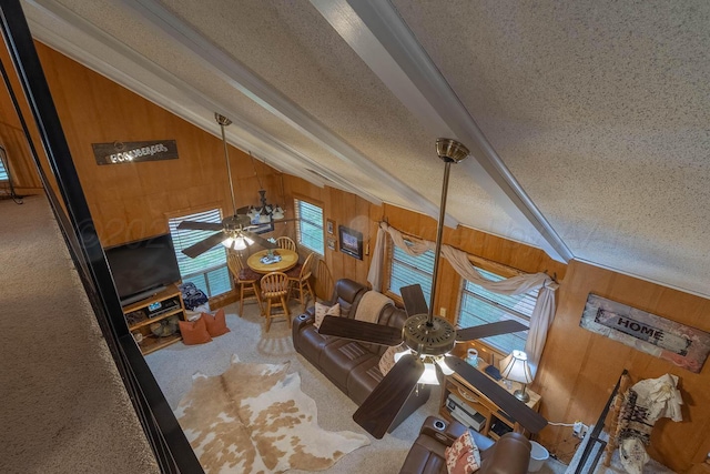 carpeted living area featuring ceiling fan, lofted ceiling, wood walls, and a textured ceiling