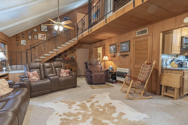 living area with heating unit, carpet flooring, high vaulted ceiling, stairs, and ceiling fan
