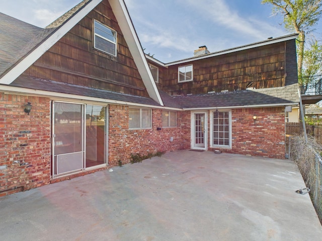 rear view of property with a patio, a chimney, fence, and brick siding