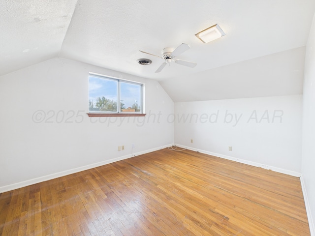 bonus room featuring light wood-style flooring, a textured ceiling, visible vents, vaulted ceiling, and baseboards