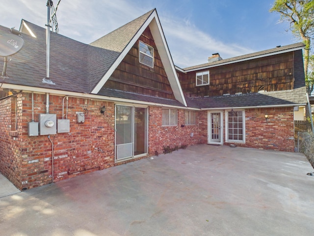 back of house with a patio, a chimney, a shingled roof, and brick siding