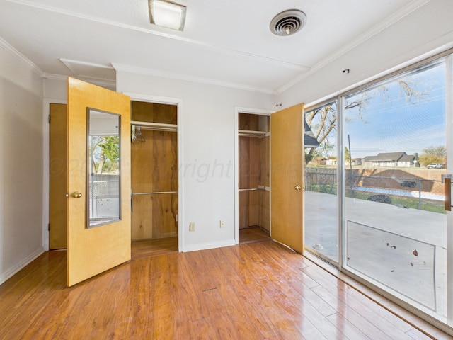 unfurnished bedroom with access to exterior, wood finished floors, multiple windows, and visible vents
