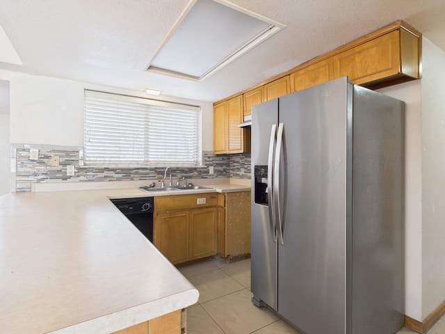 kitchen featuring black dishwasher, light countertops, a sink, stainless steel fridge, and backsplash