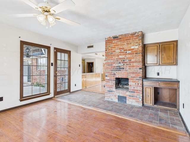 unfurnished living room featuring visible vents, a brick fireplace, wood finished floors, and baseboards