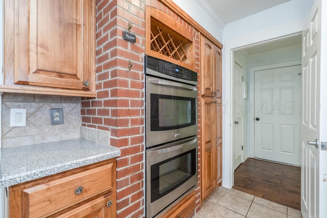 kitchen featuring backsplash, double oven, ornamental molding, light tile patterned floors, and light stone counters