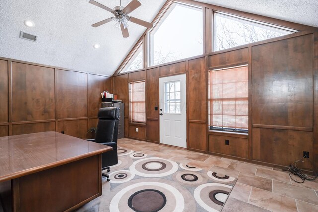 unfurnished office with visible vents, a ceiling fan, a textured ceiling, wooden walls, and vaulted ceiling