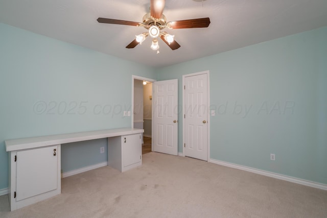 unfurnished bedroom with a ceiling fan, light colored carpet, built in desk, and baseboards